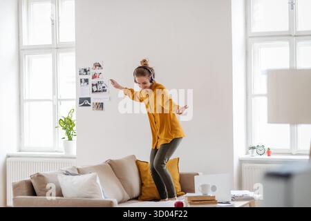 Giovane donna che balla sul divano mentre ascolta la musica. Foto Stock