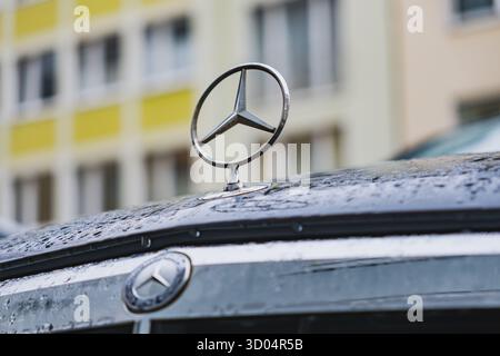 Logo Mercedes-Benz a stella a tre punte sulla parte anteriore di un'auto parcheggiata su una strada Foto Stock