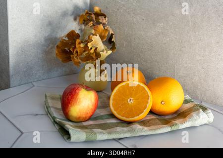 Frutta fresca di stagione mela e arancia su tagliere di legno con foglie autunnali essiccate in vaso di ceramica su piano di marmo. Nutrizione naturale sana Foto Stock