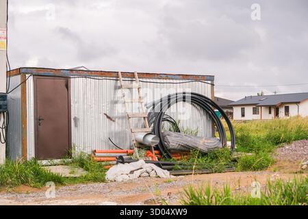Russia, San Pietroburgo, 23.08.2025 materiali da costruzione immagazzinati all'esterno di un capannone di metallo ondulato, con una scala di legno e forniture, che mostrano un edificio Foto Stock