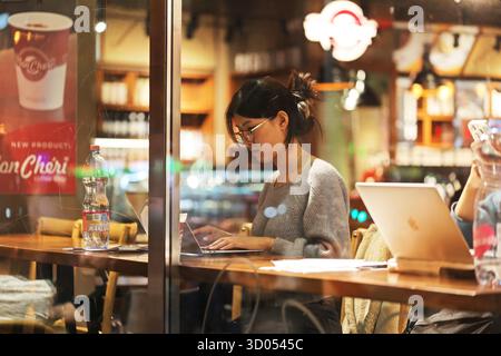 Giovane donna che lavora al suo laptop in un accogliente bar durante la sera Foto Stock