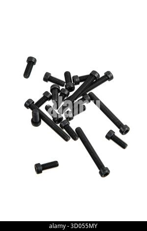 Un assortimento di viti a esagono incassato nere sparse su sfondo bianco. Foto Stock
