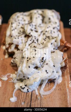 Pollo fritto con salsa cremosa di cipolla e sesamo nero, servito su un tavolo di legno. Uno spuntino fusion moderno e creativo, perfetto per bar e stuzzichini. Foto Stock