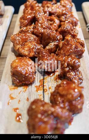Dakgangjeong verticale (pollo fritto coreano) ricoperto di salsa appiccicosa, servito su legno. Popolare snack K-Food, texture croccante. Foto Stock
