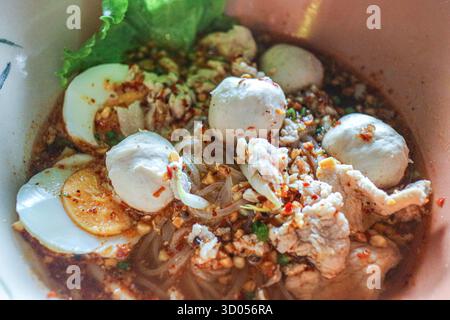 Zuppa di noodle tailandese Tom Yum piccante con maiale, polpette, uova e pasta di peperoncino. Autentico cibo di strada, ricco sapore ed essenziale pasto asiatico. Foto Stock