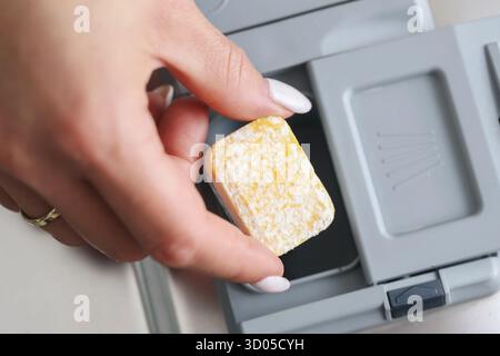 Titolo: Donna che tiene in mano un detersivo per lavastoviglie vicino al cassetto aperto. Concetto di pulizia e igiene domestica con detergente ecologico. Foto Stock