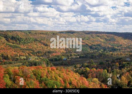 Vivace fogliame autunnale rosso arancio-giallo attraverso l'ampia valle con case di villaggio Foto Stock