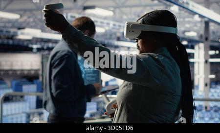 Sviluppatore di software nella sala server che indossa occhiali VR per ottimizzare le attività di gestione dei sistemi di deep learning. La donna afroamericana nel data center regola i parametri del modello di intelligenza artificiale utilizzando la realtà virtuale, la telecamera B. Foto Stock
