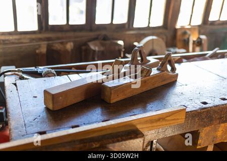 Antiche pialle manuali su banco da lavoro in legno in falegnameria. Strumenti tradizionali con luce naturale. Atmosfera rustica e autentica. Foto Stock