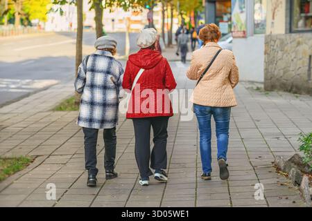Donne anziane. Tre donne anziane che camminano insieme sul marciapiede della città con caldi abiti autunnali, vista posteriore. Concetto di amicizia di alto livello e urbano di tutti i giorni Foto Stock