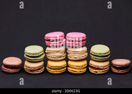 Macaron colorati assortiti impilati su righe su sfondo scuro. Il layout simmetrico crea uno stile moderno e pulito adatto per il branding degli alimenti, i pacchetti Foto Stock