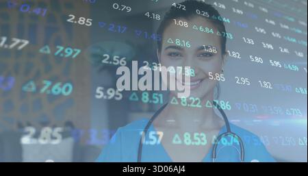 Infermiera in piedi in scrub blu indossare stetoscopio in ufficio medico, mostrando sovrapposizione dati finanziari Foto Stock