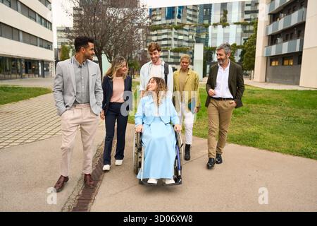 Diversi colleghi d'affari che camminano insieme a una donna in sedia a rotelle Foto Stock