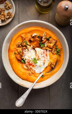 Crema di zuppa di zucca con mirtilli, noci e uovo in camicia Foto Stock