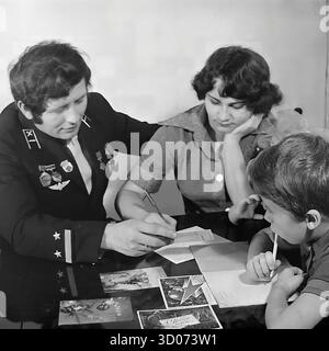 Una famiglia sovietica che scrive biglietti d'auguri natalizi a casa a Sloviansk, anni '1970-'1980 Foto d'archivio in bianco e nero, URSS, RSS Ucraina. Il padre, un macchinista e veterano nella sua uniforme ferroviaria con le medaglie, siede con sua moglie e suo figlio a un tavolo. Stanno firmando i biglietti di Capodanno o del 23 febbraio. Questa coinvolgente immagine cattura una scena della vita quotidiana sovietica, delle tradizioni familiari e dei genitori. Un documento nostalgico di una famiglia felice e di una vita pacifica nel Donbas prima della guerra. Foto Stock