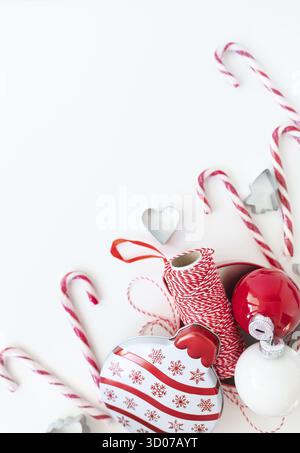 Le caramelle di Natale, insieme ai taglierini dei biscotti, ai giocattoli dell'albero di Natale ed al filo rosso per il rivestimento del regalo, si trovano su un tavolo bianco. Messa a fuoco selettiva, rumore. CHRI Foto Stock
