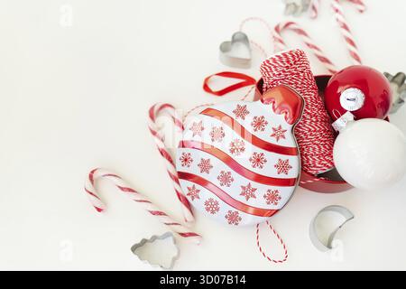 Le caramelle di Natale, insieme ai taglierini dei biscotti, ai giocattoli dell'albero di Natale ed al filo rosso per il rivestimento del regalo, si trovano su un tavolo bianco. Messa a fuoco selettiva, rumore. CHRI Foto Stock