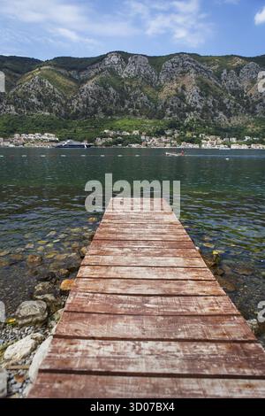 Lungo molo di legno sullo sfondo della splendida baia di Kotor, Montenegro. Il lungomare e la spiaggia erano molto belli e l'acqua era limpida e blu Foto Stock