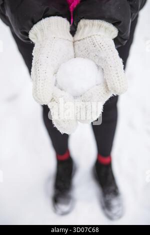 Giovane donna che tiene in mano la neve bianca morbida naturale per fare una palla di neve, giorno d'inverno nella foresta, all'aperto Foto Stock