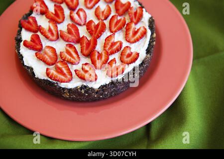 Una cheesecake alla fragola decorata con fragole a forma di cuore giace su un piatto color corallo e si erge su un tovagliolo verde. Illustrazione di un cheesec Foto Stock