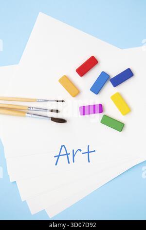 Vernici brillanti multicolore, pennelli acquerelli di diverse dimensioni si trovano insieme su carta acquerello su sfondo blu. Primo piano. L'iscrizione è Foto Stock