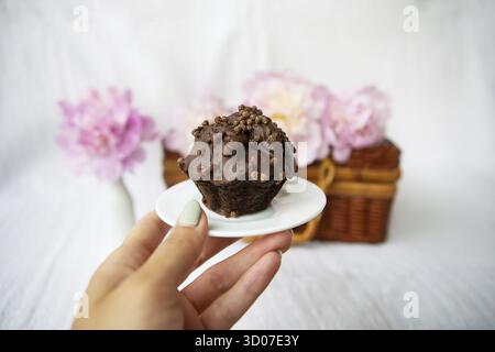 Muffin al cioccolato e bellissime peonie rosa giacciono su una valigia di legno. Bella composizione Foto Stock