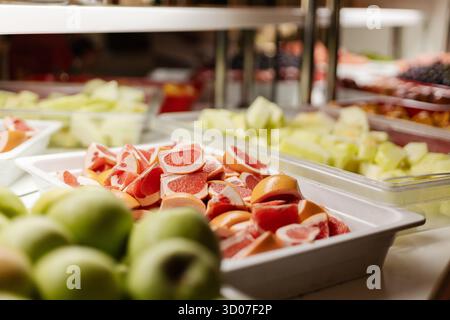 Un variopinto assortimento di frutta a fette e intera è organizzato in modo ordinato in un ambiente a buffet. Questa vivace varietà comprende meloni, mele e agrumi. Perf Foto Stock