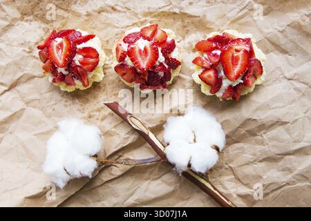 Bella tortine con le fragole insieme con un ramo di cotone si trova su carta kraft Foto Stock