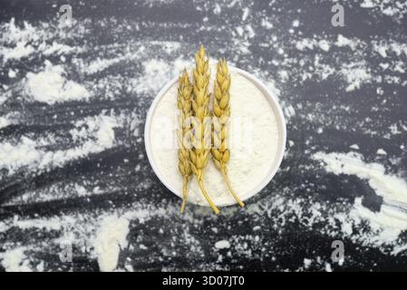 Farina di grano e orecchie in un recipiente su sfondo nero Foto Stock