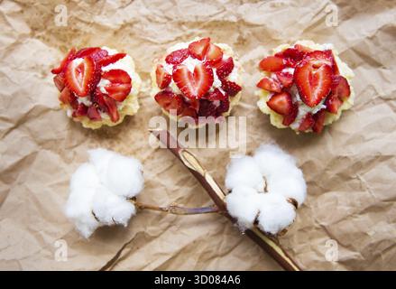 Bella tortine con le fragole insieme con un ramo di cotone si trova su carta kraft Foto Stock