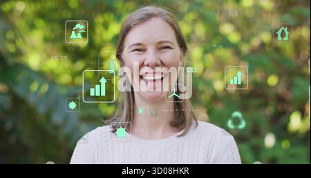 Donna sorridente che indossa un maglione in giardino con bar-chart, gocce, turbina, CO e icone di riciclaggio Foto Stock