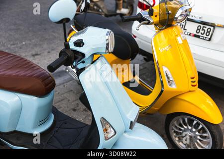 Istanbul, Turchia - 21 agosto 2025: Una vivace scena stradale presenta scooter blu pastello e giallo soleggiato parcheggiati accanto a un'auto bianca Foto Stock
