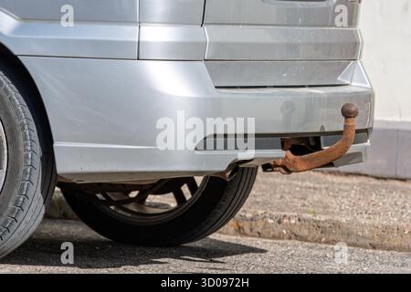 Un veicolo color argento con gancio di traino arrugginito è parcheggiato accanto al marciapiede sotto il cielo limpido. Foto Stock