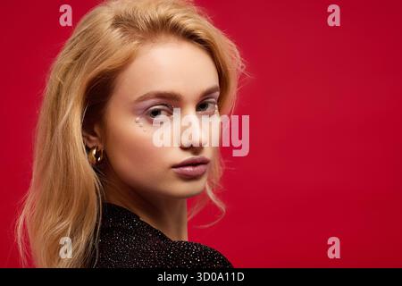 Una splendida giovane donna con un bel trucco posa graziosamente su sfondo rosso Foto Stock