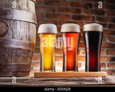 Tre bicchieri di diversi tipi di birra ghiacciata e botte di birra di legno da vicino. Foto Stock