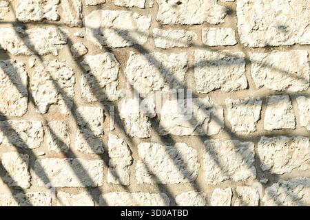 Un primo piano orizzontale di un vecchio muro di pietra ruvida, caratterizzato da sorprendenti ombre diagonali che creano un motivo astratto. Questo sfondo testurizzato offre ampio spazio di copia per progetti di grafica. Foto Stock