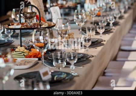 Un lungo tavolo splendidamente organizzato per un ricevimento di nozze presenta salumi, bicchieri da vino frizzante e sofisticate lenzuola grigie da tavolo, cr Foto Stock