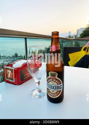 17 giugno 2025, Antalya, Turchia. Seduti in riva al mare, una bottiglia fredda di birra e un bicchiere si siedono su un tavolo mentre il sole tramonta all'orizzonte. Foto Stock