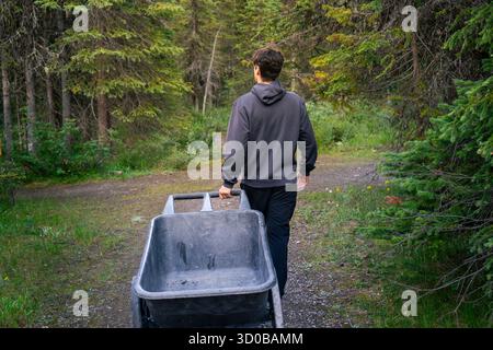 L'uomo con carriola cammina lungo i sentieri naturali in una radura forestale. Takakkaw Falls, British Columbia Foto Stock