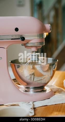 Un mixer rosa si trova su un tavolo di legno. Il mixer è argentato e ha una ciotola argentata Foto Stock