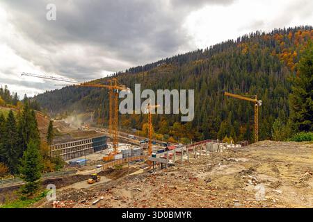Cantiere di montagna con gru multiple. Un grande cantiere in una valle di montagna con diverse gru a torre gialle e fondazioni Foto Stock