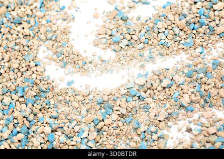 Lettiera di gatto con ciottoli blu e beige sparsi su una superficie bianca in un motivo ondulato. Sottolinea l'amore per il naturale assorbente mater Foto Stock