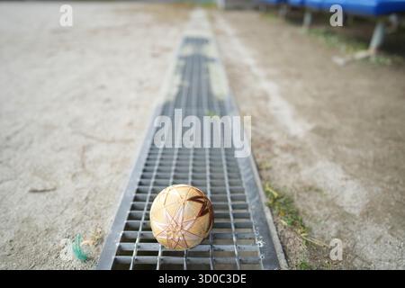 Una piccola palla è seduta su una griglia. La palla è marrone e presenta un design a foglia. La scena è ambientata sullo sfondo di un'area sabbiosa Foto Stock