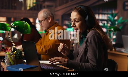 Una donna ascolta la musica ad alto volume con le cuffie e disturba le altre persone in biblioteca, un uomo anziano le chiede di mantenere basso il volume, violando le regole della biblioteca. Una persona disinteressata che canta. Foto Stock