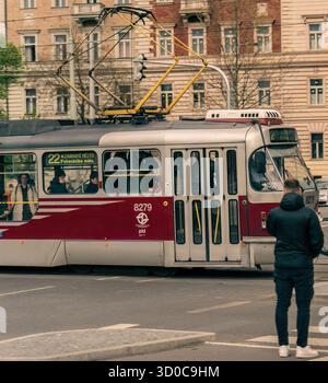 Praga, Repubblica Ceca - 23 aprile 2023: Un moderno tram viaggia attraverso una vivace strada della città, trasportando passeggeri mentre un uomo osserva nelle vicinanze. Questa città Foto Stock