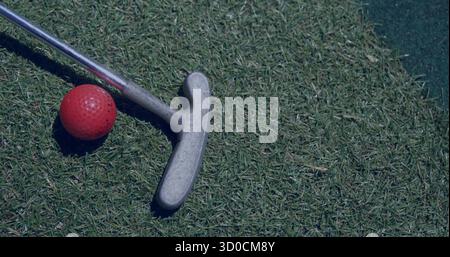 Testa di putter da golf in argento e palla da golf rossa su putting green rifinito, con tappetino sintetico Foto Stock