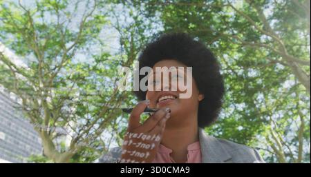 Donna con blazer grigio e camicetta rosa che esamina il pannello di visualizzazione del codice sotto la tettoia dell'albero, tenendo un marcatore Foto Stock