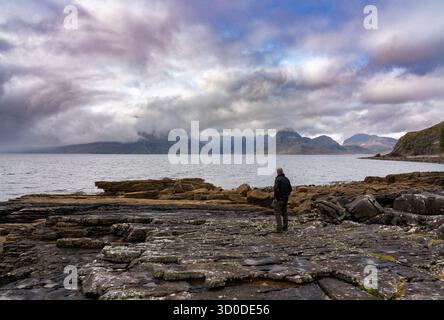lone Man si erge sulla costa rocciosa frastagliata di Elgol, sull'isola di Skye, in Scozia, guardando il mare verso le montagne coperte di nebbia Foto Stock