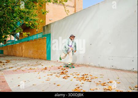 Uomo che cavalca lo skateboard sul marciapiede con foglie autunnali. Foto Stock