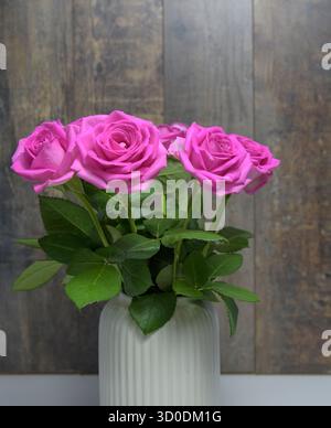 Un vaso di rose rosa siede su un tavolo di legno. Le rose sono in piena fioritura e sono disposte in modo che sembrino alte. T Foto Stock